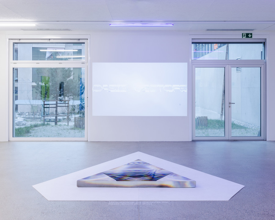 Exhibition view "F(r)ictions of Intimacy"; Soñ Gweha, RIDING APEX (OASIS VECTORS), video installation, triangular cushion and chime, dimensions variable, 2023 at CALM - Centre d'Art La Meute, Lausanne, Switzerland, 2024 / Curation Caroline Honorien / Photo: Théo Dufloo / Courtesy of the artist-x-s and CALM - Centre d'Art La Meute.