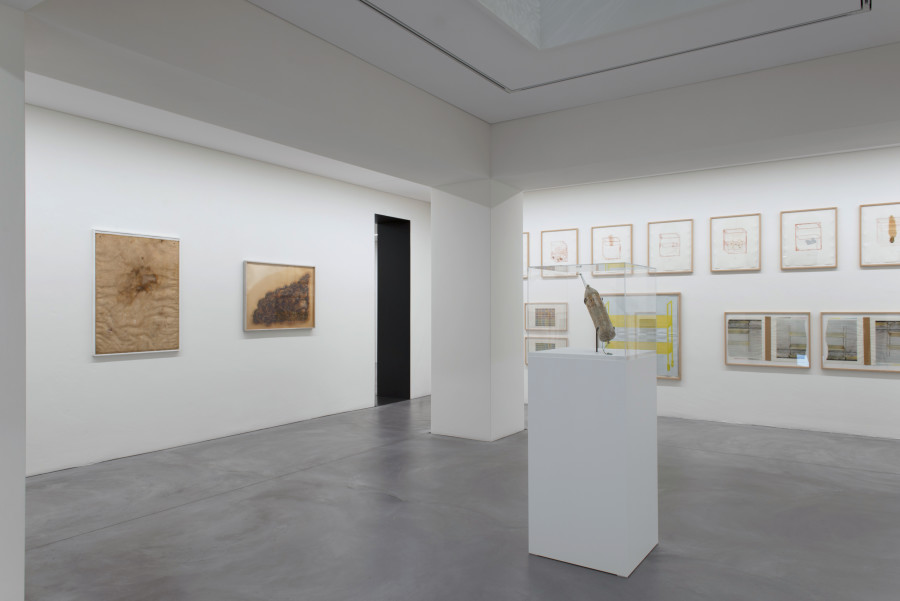 Vorne: Literaturwurst «Die Welt», 1969, (Zerhacktes Exemplar der Zeitung «Die Welt» in zu Wurst geformter Plastikhülle, Streifband), Bündner Kunstmuseum Chur, Linke Wand: Schimmelblatt, 1969, (Sauermilch auf weißem Bütten in Plastiktasche), Dieter Roth Foundation, Hamburg, © Dieter Roth Estate, Courtesy Hauser & Wirth, Large Clouds – Grosse Wolken, 1971, (Erdnussbutter und Graphit auf Papier (verschimmelt)), Bündner Kunstmuseum Chur, Rechte Wand: Div. Werke aus “Containers-Mappe”, 1972, (div. Drucktechniken), Sammlung Falckenberg