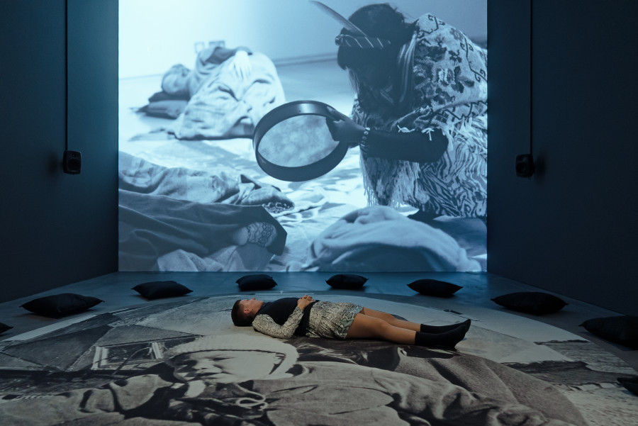 Exhibition view Interdependencies: Perspectives on Care and Resilience, Grace Ndiritu, Labour: Birth of a New Museum, 2023,Single-channel video projection (b/w, sound), Protest Carpet: MOTHERHOOD, 2022, Printed woven carpet. Courtesy the artist and Kate MacGarry, London. Commissioned by RAMM, Exteter. Photo: Studio Stucky