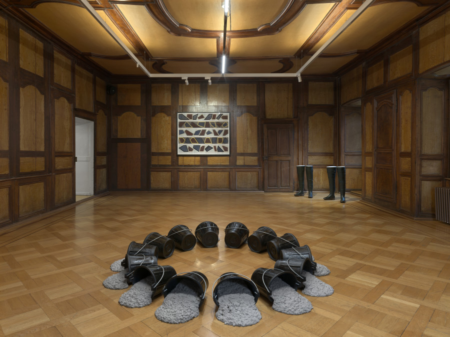 Vue de l’exposition C’EST BIZ’ART, Le Manoir de la Ville de Martigny, Valais, 2025. Delphine Reist, Rond de seaux, 2025, caoutchouc naturel et béton ; David Tremlett, Roll On #9, 2016, pastel sur papier ; Delphine Reist, Grandes bottes, 2017, bottes de pêche et béton. © Annik Wetter