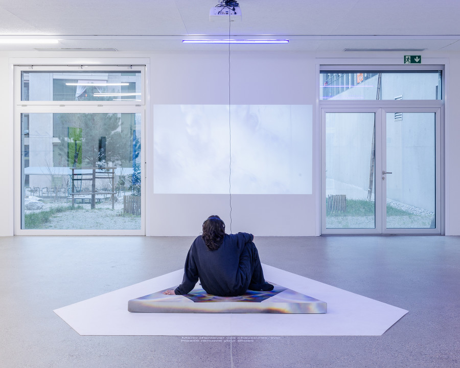 Exhibition view "F(r)ictions of Intimacy"; Soñ Gweha, RIDING APEX (OASIS VECTORS), video installation, triangular cushion and chime, dimensions variable, 2023 at CALM - Centre d'Art La Meute, Lausanne, Switzerland, 2024 / Curation Caroline Honorien / Photo: Théo Dufloo / Courtesy of the artist-x-s and CALM - Centre d'Art La Meute.